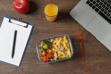 Lezzetli yiyecek, çatal, dizüstü bilgisayar, bir bardak meyve suyu, ahşap masa üzerinde elma ve pano, düz yatak. İş yemeği.