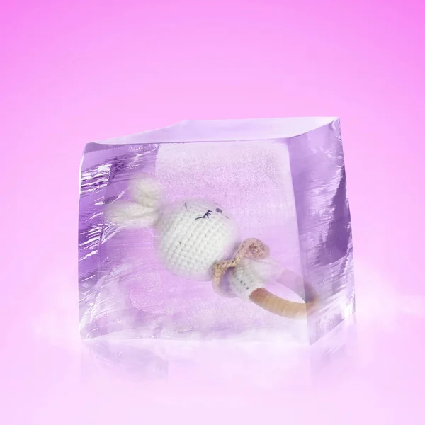Conservation of genetic material. Baby teether toy in ice cube as cryopreservation on violet background