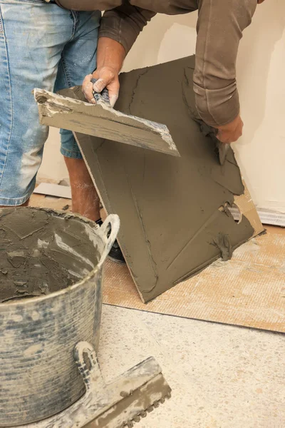 Worker spreading adhesive mix over tile with spatula, closeup