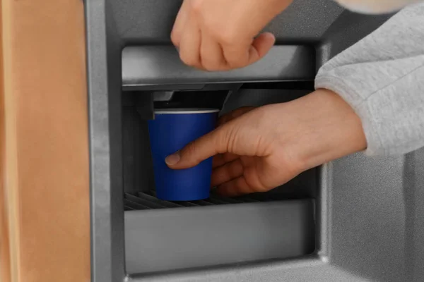 Woman taking paper cup with coffee from vending machine, closeup