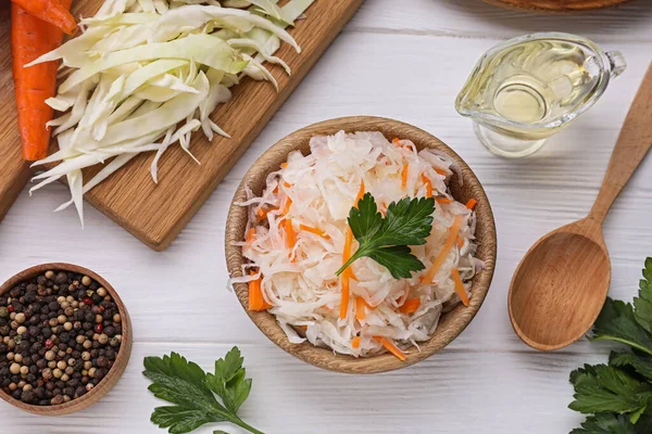 stock image Bowl of tasty sauerkraut and ingredients on white wooden table, flat lay