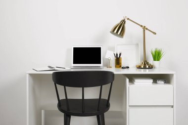 Evdeki ahşap masada dizüstü bilgisayarı, lambası ve kırtasiyesi olan rahat çalışma alanı.