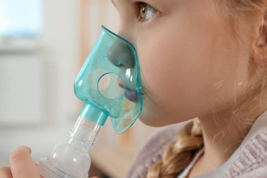 Little girl using nebulizer for inhalation indoors, closeup
