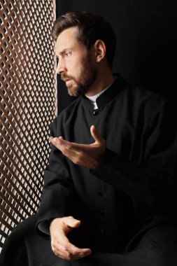 Cüppeli Katolik bir rahip günah çıkarma kabininde cemaatle konuşuyor.