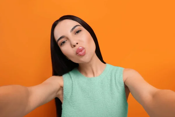 Piękna Młoda Kobieta Biorąc Selfie Podczas Wieje Pocałunek Pomarańczowym Tle — Zdjęcie stockowe