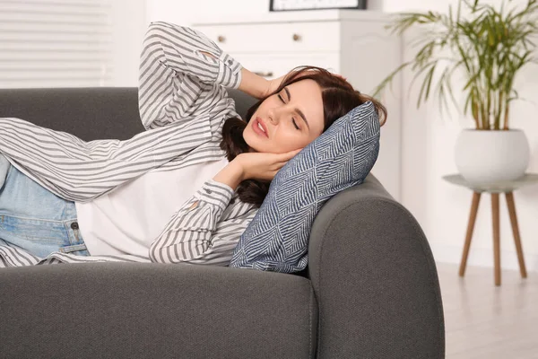 Young woman suffering from headache on sofa indoors. Hormonal disorders