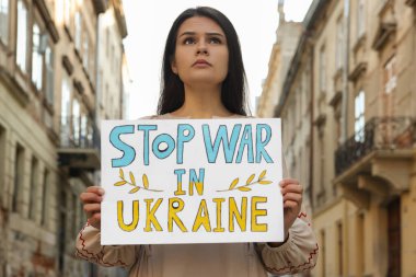 Sad woman holding poster Stop War in Ukraine on city street