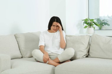 Young woman suffering from headache on sofa at home. Hormonal disorders