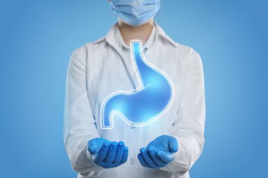 Mide ekşimesinin ve diğer gastrointestinal hastalıkların semptomları. Açık mavi arkaplanda mide illüstrasyonunu tutan doktor, yakın plan.