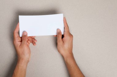 Man holding flyer on grey background, closeup. Mockup for design