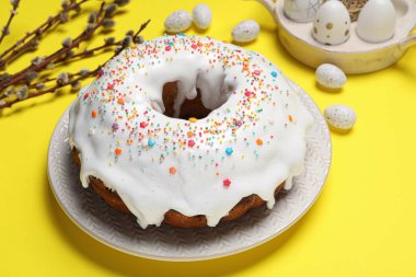 Easter cake with sprinkles, painted eggs and willow branches on yellow background