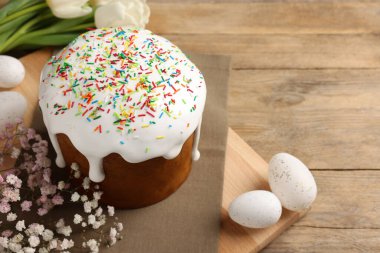 Tasty Easter cake, decorated eggs and flowers on wooden table. Space for text