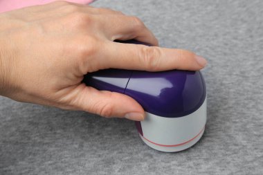 Açık gri kumaş üzerinde kumaş traş makinesi kullanan bir kadın.