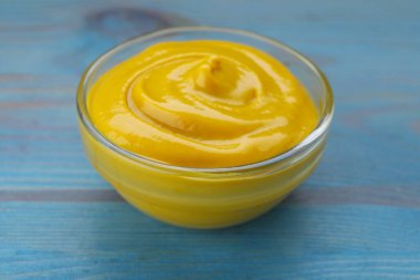 Açık mavi ahşap masada leziz hardallı sos kasesi, yakın plan.