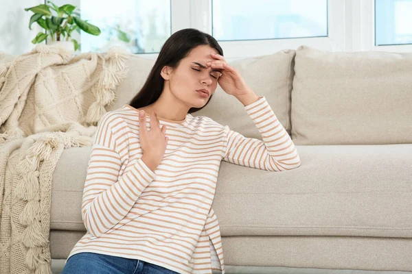 Young woman suffering from headache near sofa indoors. Hormonal disorders