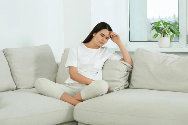 Young woman suffering from headache on sofa at home. Hormonal disorders