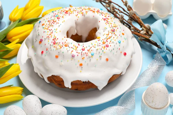 精美的复活节蛋糕 装饰在美丽的郁金香 柳枝和浅蓝色背景彩绘的彩蛋旁边 点缀着小花 — 图库照片