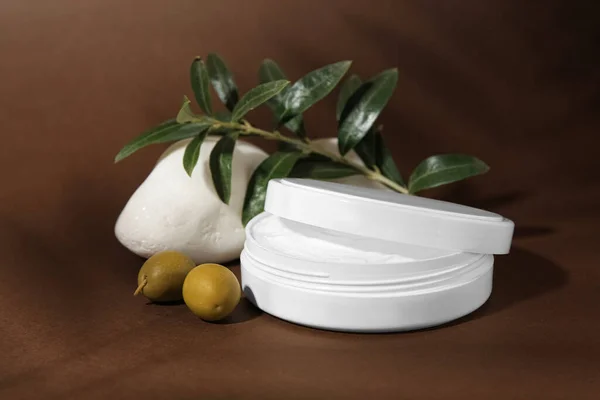 Jar of natural cream, stone and olives on brown background. Cosmetic products