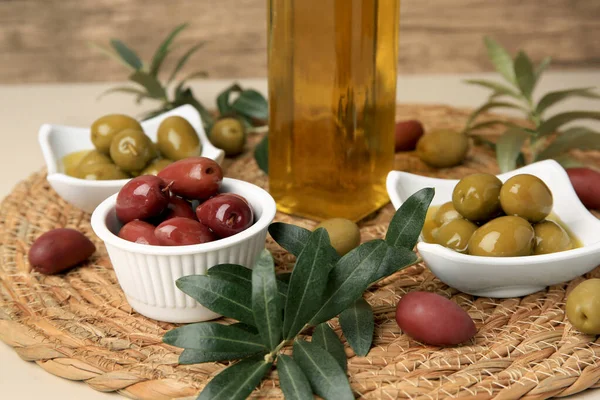 Bottle of oil, olives and tree twigs on table