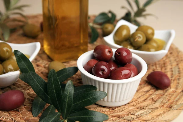 Bottle of oil, olives and tree twigs on table, closeup
