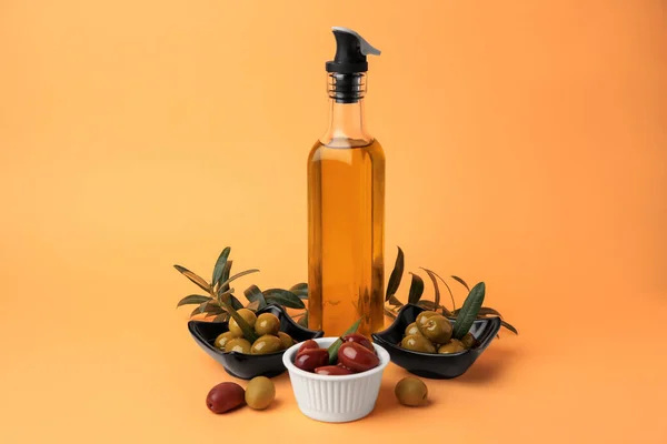 Bottle of oil, olives and tree twigs on orange background