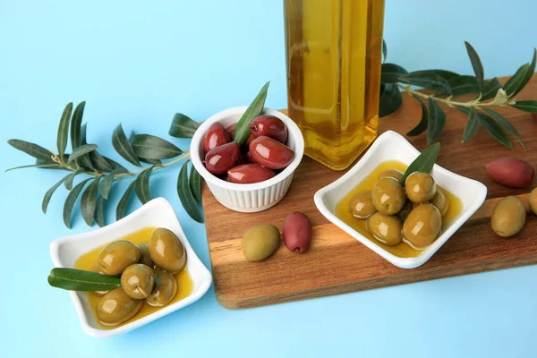 Bottle of oil, olives and tree twigs on light blue background