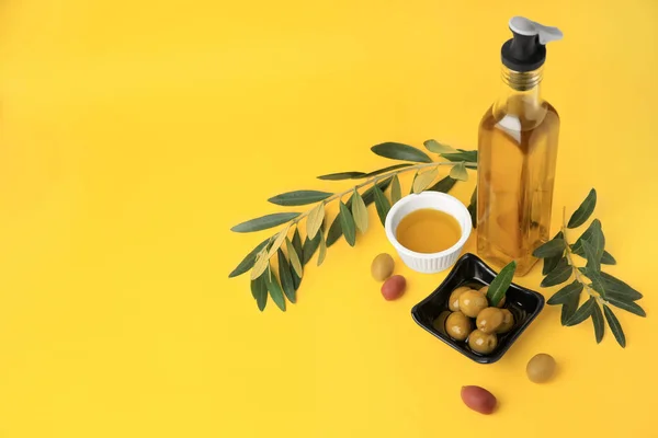 Oil, olives and tree twigs on yellow background, space for text
