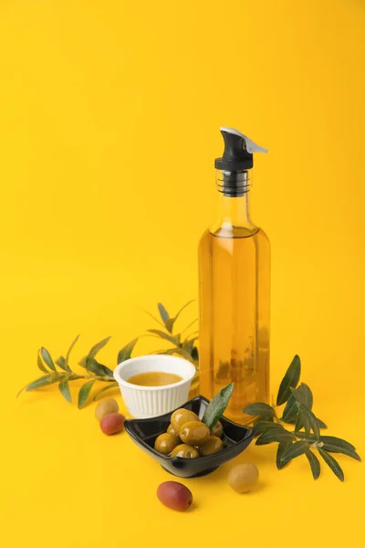 Oil, olives and tree twigs on yellow background