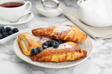 Fresh tasty puff pastry with sugar powder and blueberries served on white marble table, closeup