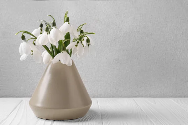 stock image Beautiful snowdrops in vase on white wooden table, space for text