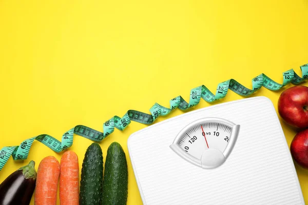 Scales, measuring tape, fresh vegetables and apples on yellow background, flat lay with space for text. Low glycemic index diet