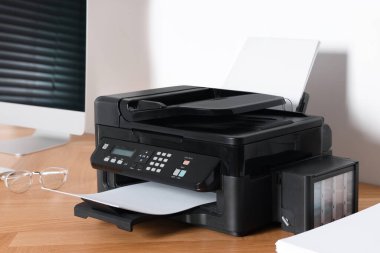 Ofisteki ahşap masadaki bilgisayarın yanında kağıdı olan modern yazıcı