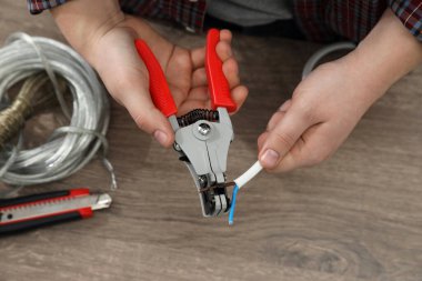 Professional electrician stripping wiring at wooden table, above view