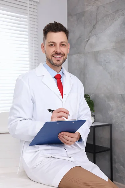Happy doctor with clipboard and pen in clinic