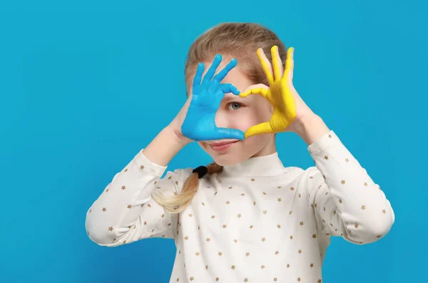 stock image Little girl making heart with her hands painted in Ukrainian flag colors on light blue background, space for text. Love Ukraine concept