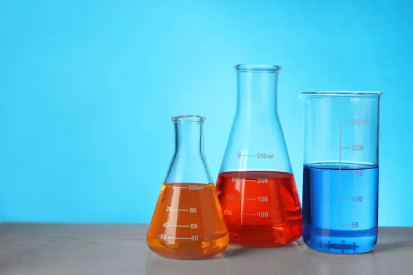 Glazen Kolven Met Kleurrijke Vloeistoffen Houten Tafel Tegen Lichtblauwe Achtergrond — Stockfoto