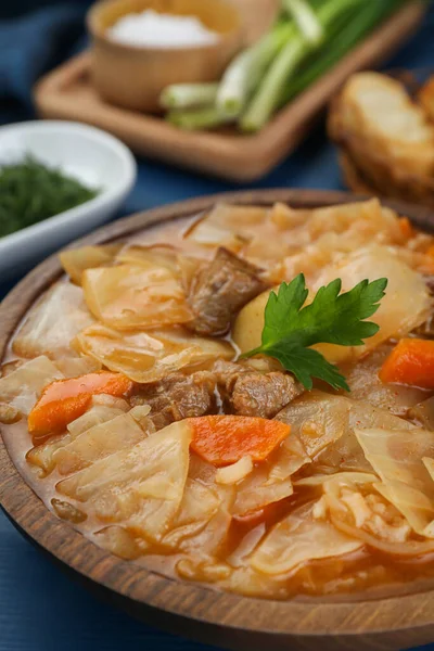 Tasty cabbage soup with meat, carrot and parsley on blue wooden table, closeup