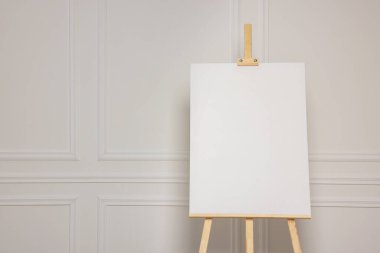 Beyaz duvarın yanında boş tuval olan tahta sehpa. Metin için boşluk