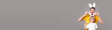 Tavşan kulaklıklı baba ve oğul gri arka planda eğleniyor, mesaj için yer var. Paskalya kutlaması, pankart tasarımı