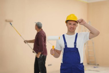 Worker holding paint roller in unfinished room. Painting walls