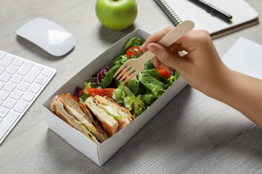 Ofis çalışanı beyaz ahşap masada taze salata yiyor, yakın plan. İş yerinde iş yemeği.