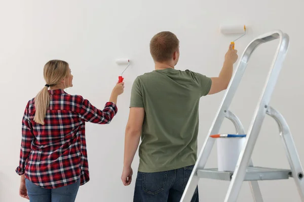Couple painting wall in apartment during repair, back view