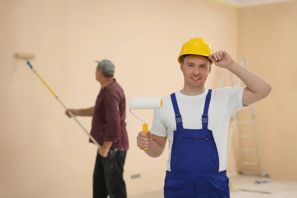 Worker holding paint roller in unfinished room. Painting walls