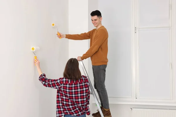 Young couple painting wall with rollers indoors. Room renovation