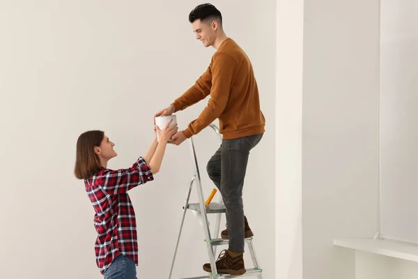 Young Woman Giving Paint Can Boyfriend Stepladder Indoors Room Renovation — Stockfoto