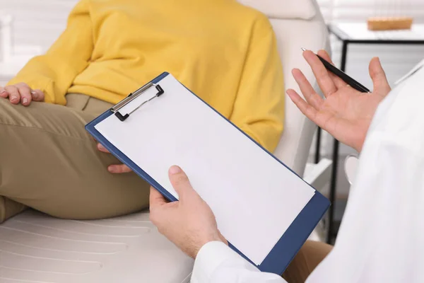 Doctor with clipboard consulting patient in clinic, closeup