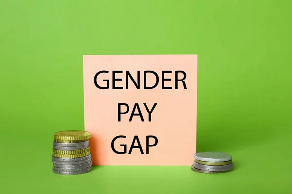 Gender pay gap. Paper note and stacked coins on light green background