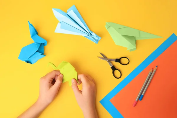 stock image Origami art. Child holding paper figures on yellow background, closeup and top view