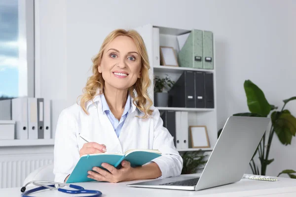 Doctor with laptop and notebook at desk in clinic. Online medicine concept
