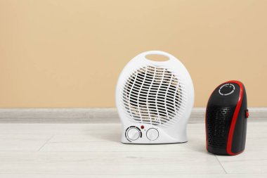 Bej duvarın yanındaki zeminde modern elektrikli kompakt ve fan ısıtıcıları, metin için yer